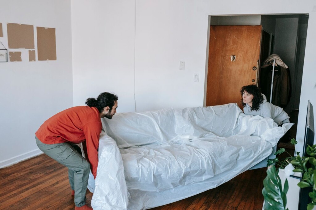 هل نقل العفش يشمل الفك والتركيب؟ خبراء نقل الأثاث A couple collaboratively lifting a couch while moving into a new apartment.